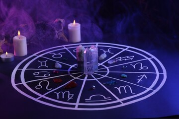Natural stones for zodiac signs, drawn astrology chart and burning candles on dark blue table....