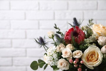 Beautiful bouquet with roses against white brick wall, closeup. Space for text