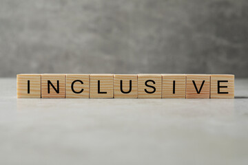 Wooden cubes with word Inclusive on grey table against blurred background