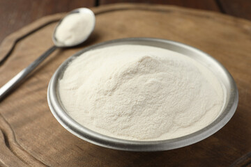 Bowl and spoon of agar-agar powder on wooden table, closeup