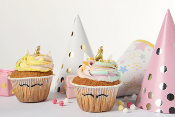Cute sweet unicorn cupcakes and party hats on white table