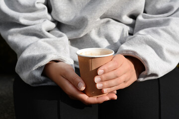 Woman sitting with cardboard cup of coffee, closeup