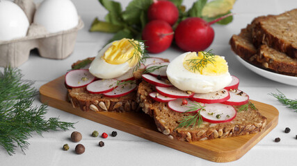 Fototapeta na wymiar Tasty sandwiches with boiled egg, radish and ingredients on white tiled table