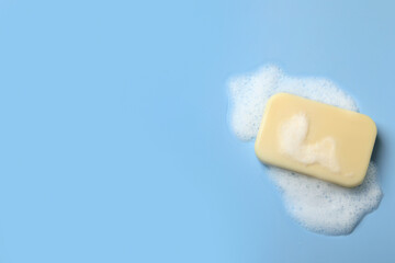 Soap and fluffy foam on light blue background, top view. Space for text