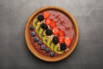 Bowl of delicious smoothie with fresh blueberries, strawberries, kiwi slices and blackberries on grey table, top view