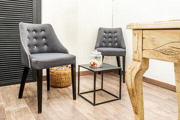 Waiting room with two gray fabric stools with buttons and a small table with courtesy trinkets