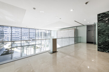 Atrium of an office building with green marble tiled walls, cream marble floors viewed from a large mezzanine window with a glass railing and a revolving door at the entrance - obrazy, fototapety, plakaty