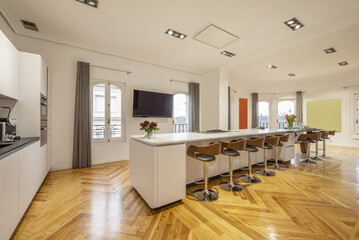 A large center island filled with metal and wood stools in a kitchen with pine stained hardwood flooring