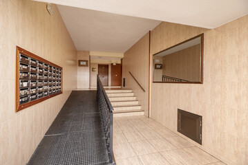 Portal of a residential housing building with a ramp for the disabled, a string of mailboxes and imitation marble tiling on walls and floors