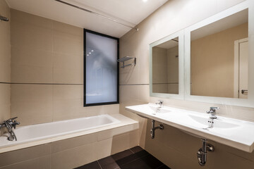 bathroom with double sink in a single piece of porcelain and chrome plumbing. Twin frameless mirrors on the wall and long tub on one side