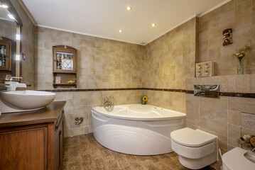 Bathroom with country-style porcelain sink over wood cabinet and quarter-circle whirlpool tub and tonal tile with valance