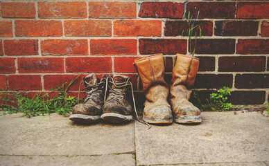 Two pairs of old boots in front of a  brick wall.The boots are heavily worn steel toe cap safety...