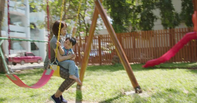 Asian boy Playing on the swings at the playground with parents.