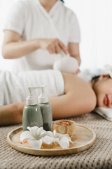 Obraz na płótnie Canvas Relaxed pretty asian young woman enjoying remedial body massage done by professional masseur in spa room, with herbal compress balls in therapy spa salon.