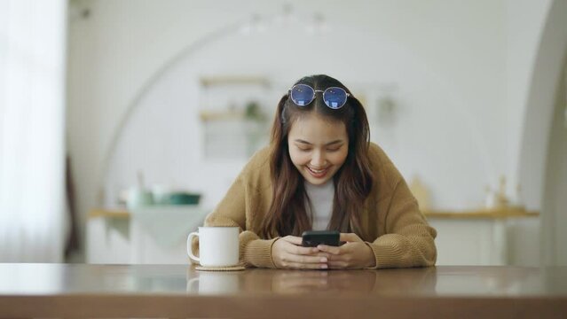 Excited asian female using mobile smart phone. Young asia woman happy and smiling at house
