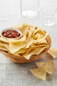Tortilla Chips and Bowl of Salsa in Wicker Basket on Grey Background with Empty Glasses, Studio Shot