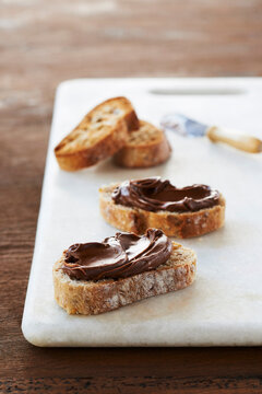 Slices of Baguette topped with Hazelnut Spread on Marble Slab on Wooden Background, Studio Shot