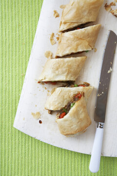 Savoury vegetable strudel, sliced on a white board with knife, against a green background