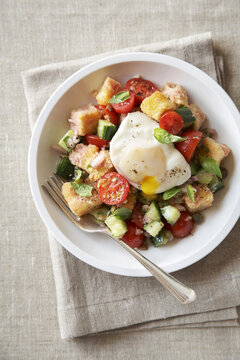 Panzanella bread salad with a poached egg in a white bowl on a beige linen background