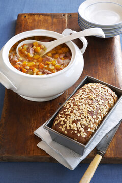 Ham hock soup served with multigrain bread on a wooden cuttting board with blue linen tablecloth