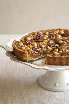 Mixed nut tart on a crockery cake stand with a slice being served