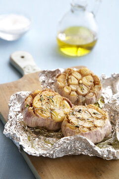 Roasted garlic bulbs with herbs and olive oil in tin foil on a cutting board