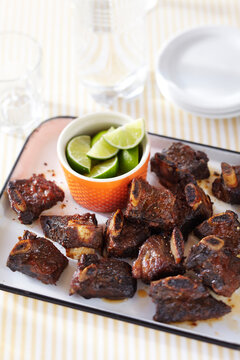 Beef Ribs with spice rub, served with lime wedges on a platter