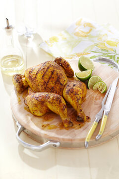 Spatchcock grilled chicken with spice rub on wooden cutting board and lime wedges