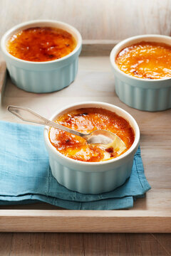 Three ramekins of creme brulee on a wooden tray