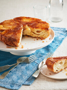 Kouign Amann on a cake stand with a piece taken out and served on dessert plate with forks in front