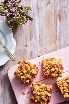 Four plum oat squares on a pink wooden board with purple flowers