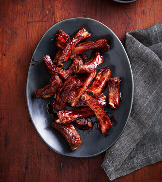 Platter of barbecued ribs with glaze on a wooden background