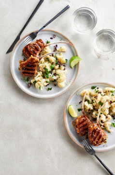 Two plates of grilled lamb chops with cauliflower salad on a grey background