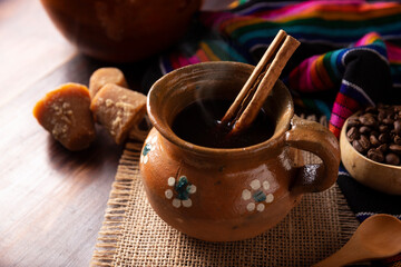 Authentic homemade mexican coffee (cafe de olla) served in traditional handmade clay mug (Jarrito de barro) on rustic wooden table.