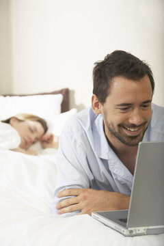 Couple in Bed, Man Using Laptop