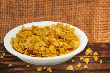 bowl of cornflakes on wooden table with blurred jute cloth background.