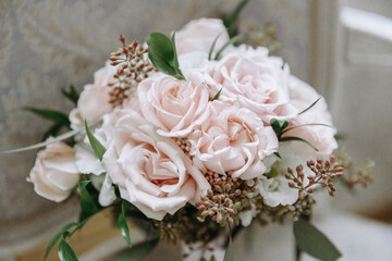 A wedding bouquet of white roses in an expensive interior lies on a chair,festive ribbons on the bouquet, details at the wedding, the bride's bouquet