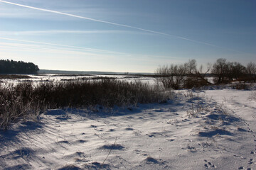 Fototapeta na wymiar Bright sunny winter day. Blue sky and snow-covered coast. A contrast view from the coast for the beginning of the Vileysky reservoir in Belarus.