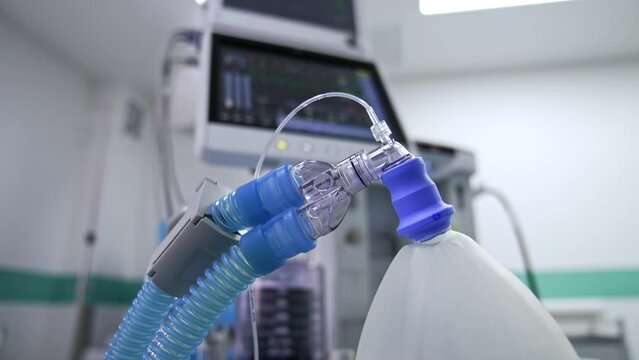 The ambu bag with two thick tubes connected. Close up. Lung ventilation machine at backdrop in blur.