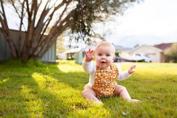 Happy baby with hand up giving high five outside on grass