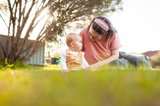 Low angle view of young mum and baby sitting on front lawn grass on spring afternoon