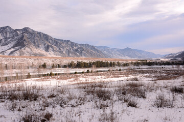 Snow-covered valley with low dry grass surrounded by high mountains in early winter.