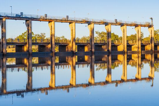 The flood gates of a tall weir reflected in the water of a calm river