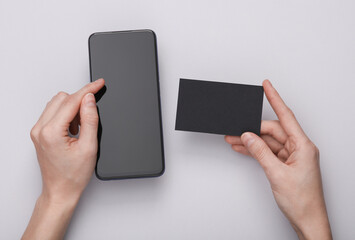 Woman's hand uses a smartphone and holds a business card on a gray background