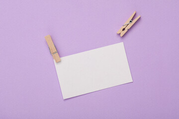 Blank business card and clothespins on purple background. Mockup for presentations and corporate identity