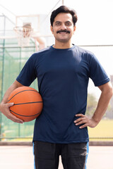 Portrait of a young man holding a basketball ball at the outdoor courtyard.