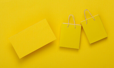Yellow business card for your brand and mini shopping bags on yellow background. Shopping, sale concept