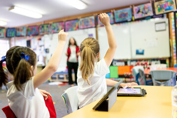 Two Students with Hands Up on iPads in Classroom