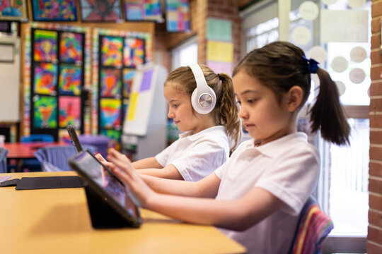 Two Young Schoolgirls on iPads in Classroom