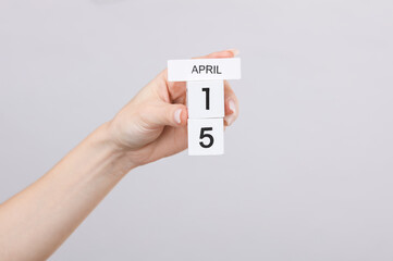 Block calendar with date april 15 in female hand on gray background